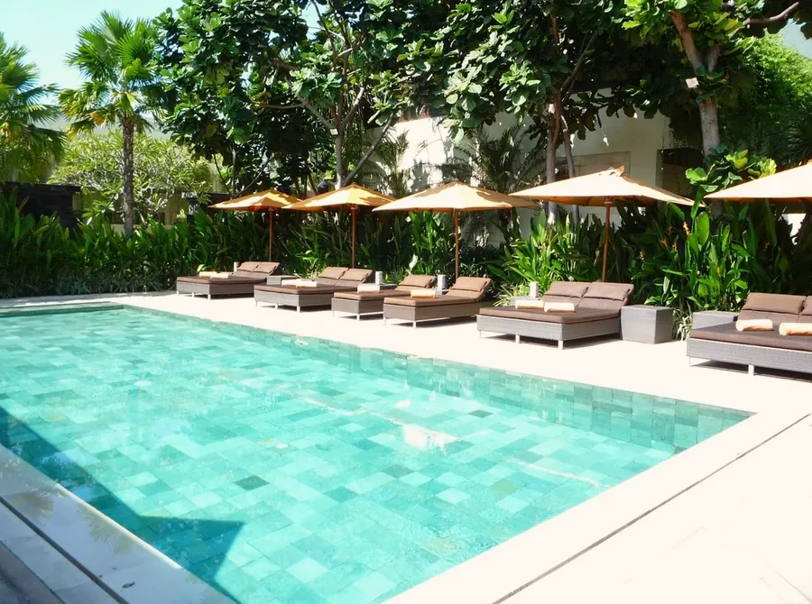 A turquoise pool with sun loungers and parasols